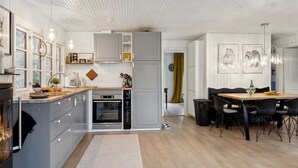 Une cuisine moderne avec des meubles gris, un four encastré et un coin repas comprenant une table en bois et des chaises noires.