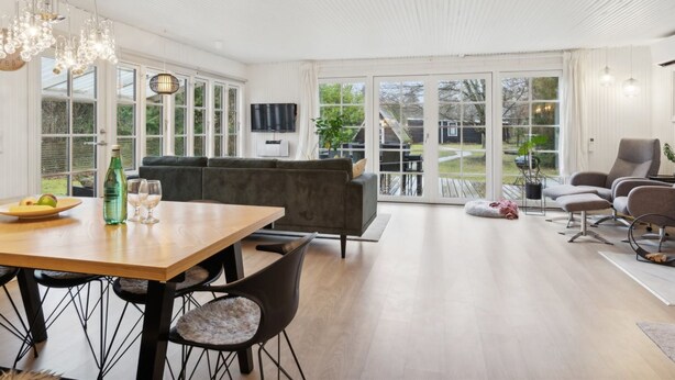 Un vaste espace de vie comprenant une table à manger en bois, des canapés foncés et une grande fenêtre donnant sur l’extérieur.