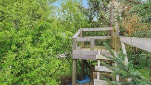 Une structure de jeux en bois avec un toboggan, située dans une zone boisée.