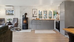 Une cuisine moderne avec des meubles gris, un poêle à bois et une grande fenêtre donnant sur un paysage enneigé.