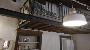 A room with exposed wooden beams, a hanging light fixture, and a bookshelf with books and decorative items. - Loft - Le Maioliche (Montelupo Fiorentino)