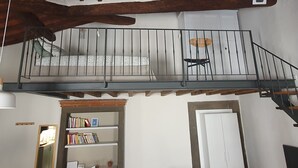A loft-style room with a wooden ceiling, a balcony with a metal railing, a bookshelf, and a door. - Loft - Le Maioliche (Montelupo Fiorentino)