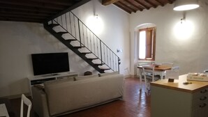 A living room with a sofa, a TV, a staircase, and a kitchen area with a table and chairs. - Loft - Le Maioliche (Montelupo Fiorentino)