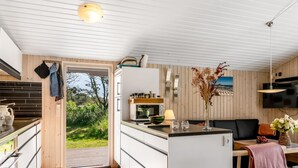 Eine moderne Küche mit weißen Schränken, einer Mikrowelle und einem Spülbecken. Ein Essbereich mit Tisch und Stühlen bietet einen Blick ins Freie.