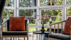 Ein Zimmer mit großen Fenstern, einer Holzdielen-Terrasse und zwei Sesseln mit Kissen.