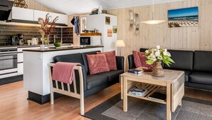 Ein zeitgemäßer Wohnraum mit einer Küche, einem schwarzen Sofa, einem Holztisch und Meerblick durch ein Fenster.