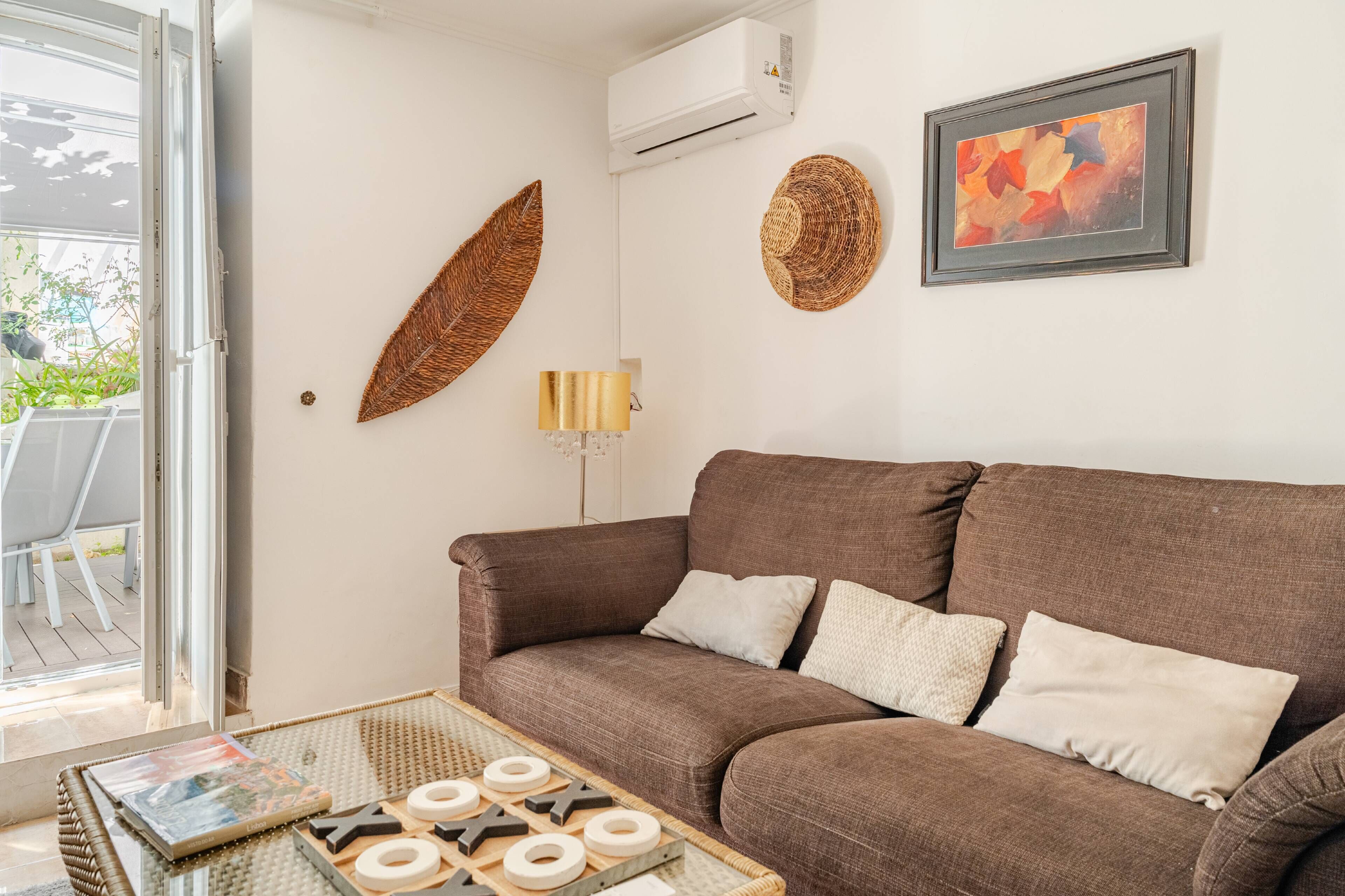 Un salon avec un canapé marron, une table basse en verre agrémentée d’objets décoratifs, une décoration murale en osier, une lampe fixée au mur et un tableau abstrait encadré.
