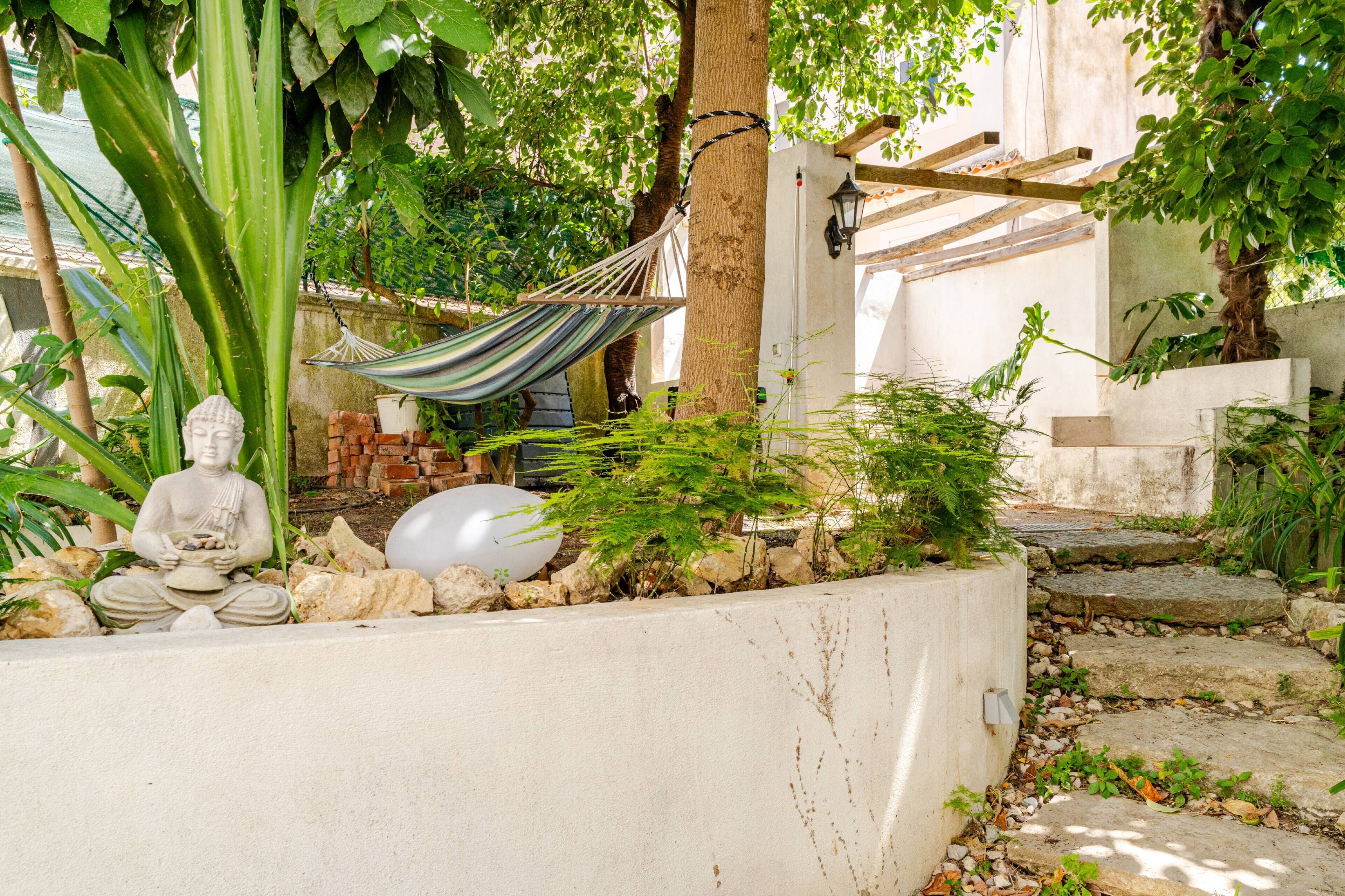 Un jardin paisible avec une statue de Bouddha, un hamac et un mur blanc.