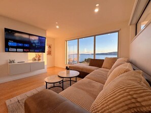 Ein modernes Wohnzimmer mit großem Flachbildfernseher, einer Couch, einem Couchtisch und Blick auf das Meer.