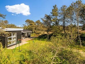 Une maison moderne dotĂ©e dâune grande fenĂȘtre, dâun patio et dâune balançoire, le tout situĂ© dans un cadre naturel.