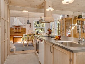 Eine Küche mit Holzausstattung, einer großen Kochinsel mit Spüle, Pendelleuchten und einer Segelboot-Dekoration.