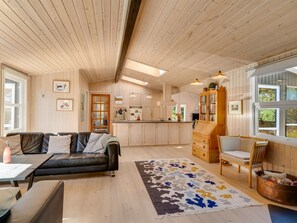 LâintĂ©rieur chaleureux dâun chalet avec un plafond en bois, un coin cuisine, un salon dotĂ© dâun canapĂ© et dâune table basse, et un coin repas avec une table et des chaises.