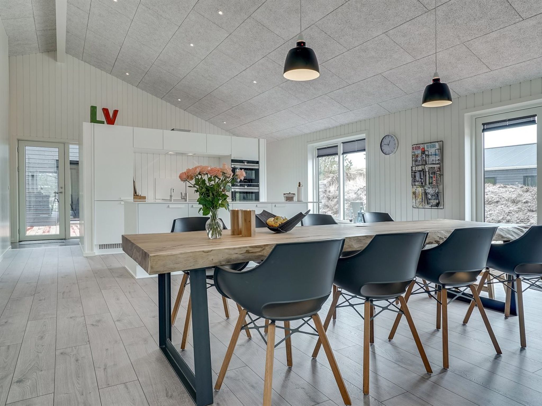 Una cocina moderna con armarios blancos, una mesa de comedor de madera con seis sillas e iluminación colgante.