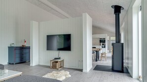 A modern living room with a flat-screen TV, a fireplace, and a kitchen in the background. - "Helli" - 650m from the sea by Interhome (Thisted)