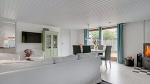A modern living room with a large white sofa, a dining area with a table and chairs, a green cabinet, and a fireplace. - "Landolf" - 250m from the sea by Interhome (Hals)