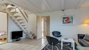 En moderne stue med trappe, et fladskærms-tv, et spiseområde med bord og stole, samt en sofa.