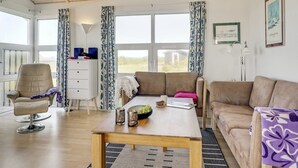 A spacious room with a wooden ceiling, large windows, a sofa, a dining table, and a chair.