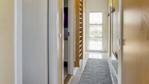 A hallway with a wooden staircase, a door with a metal handle, and a window with blinds.