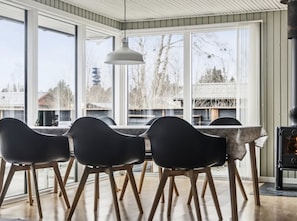 Un comedor con mesa y sillas, ventanas amplias y una estufa de leña.