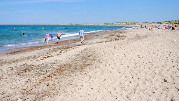 A sandy beach with people walking and swimming.