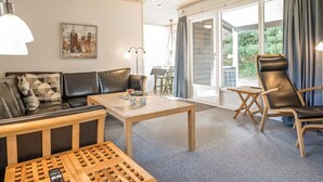 A modern living room with a sofa, coffee table, and a chair. There is a painting on the wall and a view of the outdoors through a sliding door.