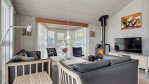Uma sala de estar moderna com sofá, mesa de jantar e televisão. Há uma lareira e um quadro na parede.