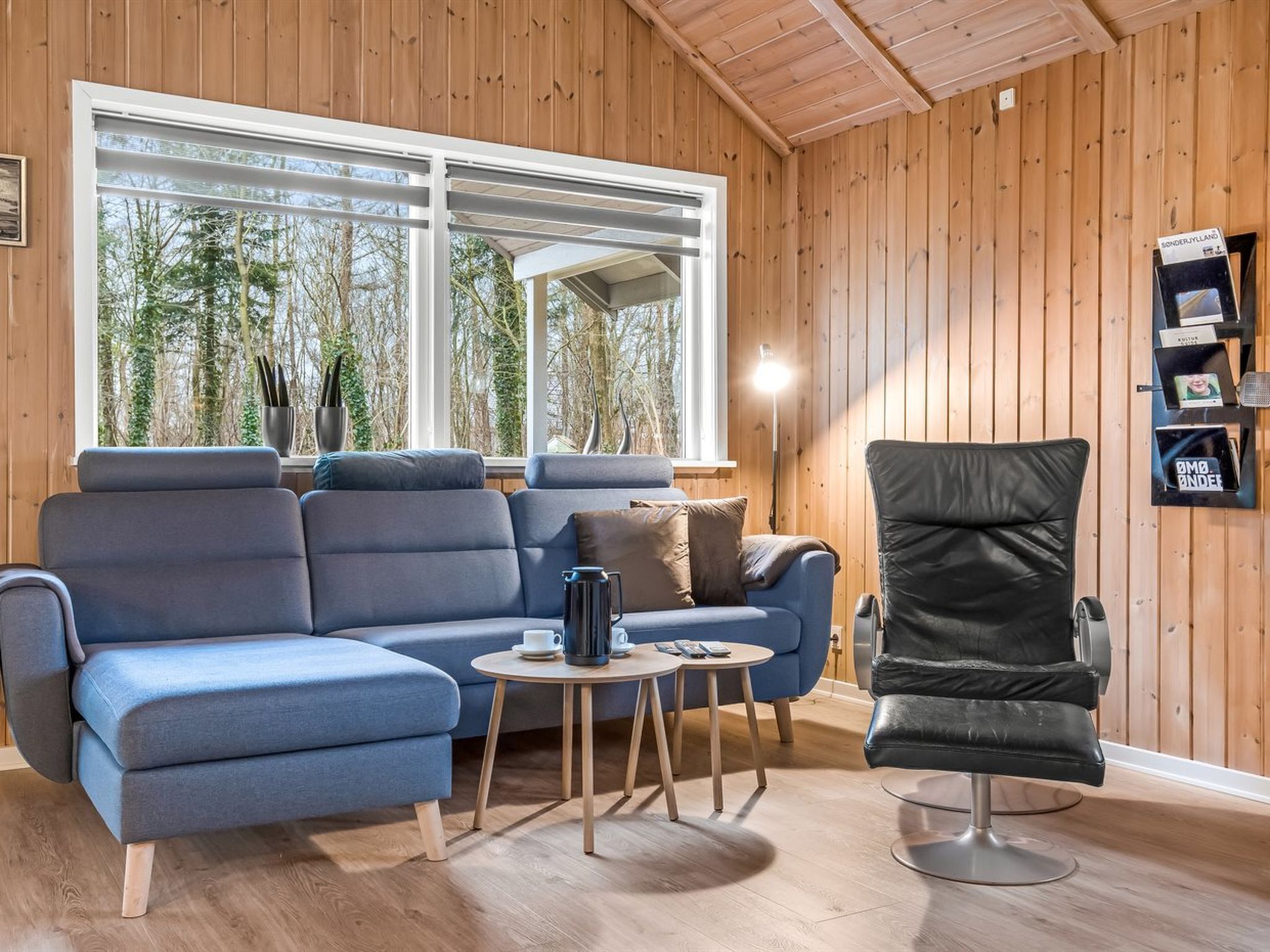 Ein modernes Wohnzimmer mit einem blauen Sofa, einem schwarzen Sessel und einem kleinen Tisch mit einer Kaffeekanne.