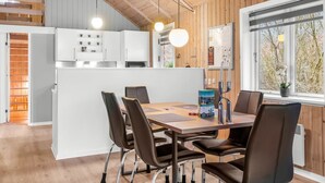 Et moderne køkken med hvide skabe, loft i træ og et spiseområde med et træbord og stole.