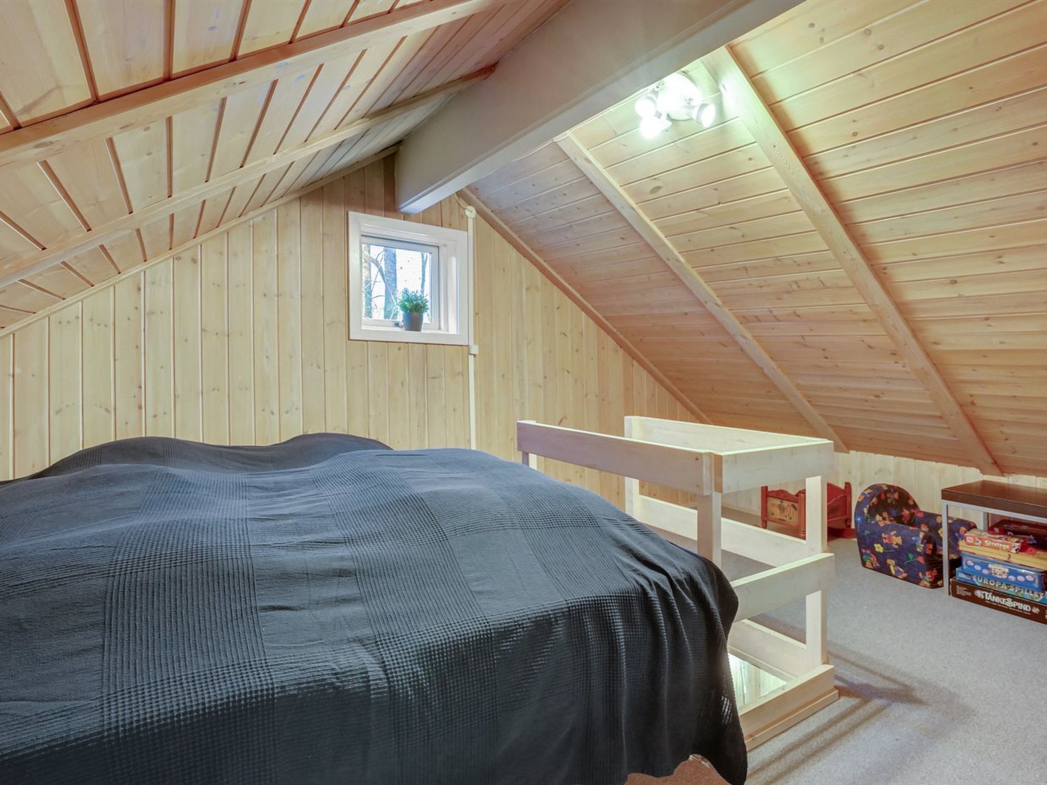 Ein gemütliches Schlafzimmer im Dachgeschoss mit einem Etagenbett, einem kleinen Fenster und einer Holzbalkendecke.