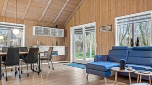Et moderne interiør med træloft, spiseplads med stole og bord, en blå sofa og et køkken med skabe og et vindue.