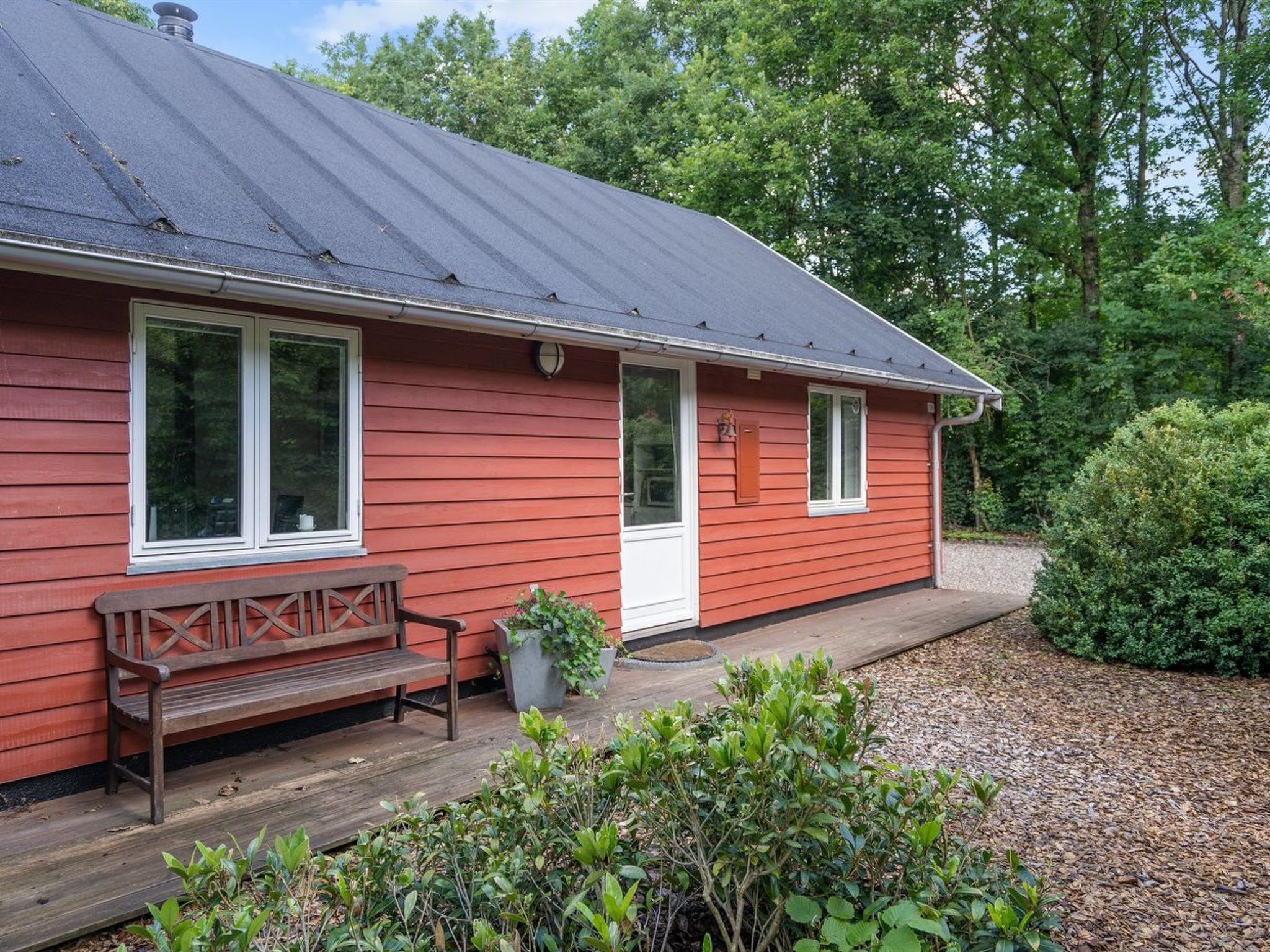 Una casa de madera roja con un porche, un banco y un pequeño jardín.
