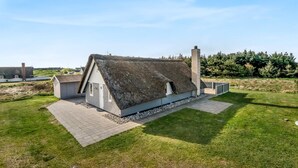 Een rieten dak huis met schoorsteen, omringd door een gazon en een geplaveid pad.