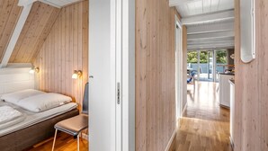 Een moderne, compacte kamer met een schuine kap, houten wanden, een bed met hoofdeinde, een bankje, en een deur naar een buitenruimte met een tafel en stoelen.