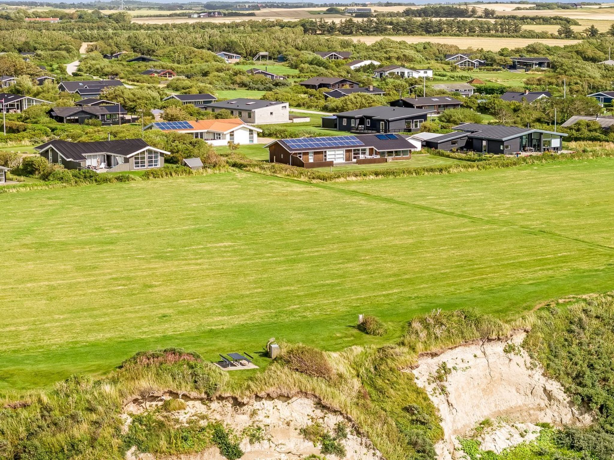 A residential area with houses, a large green field, and a sandy area.