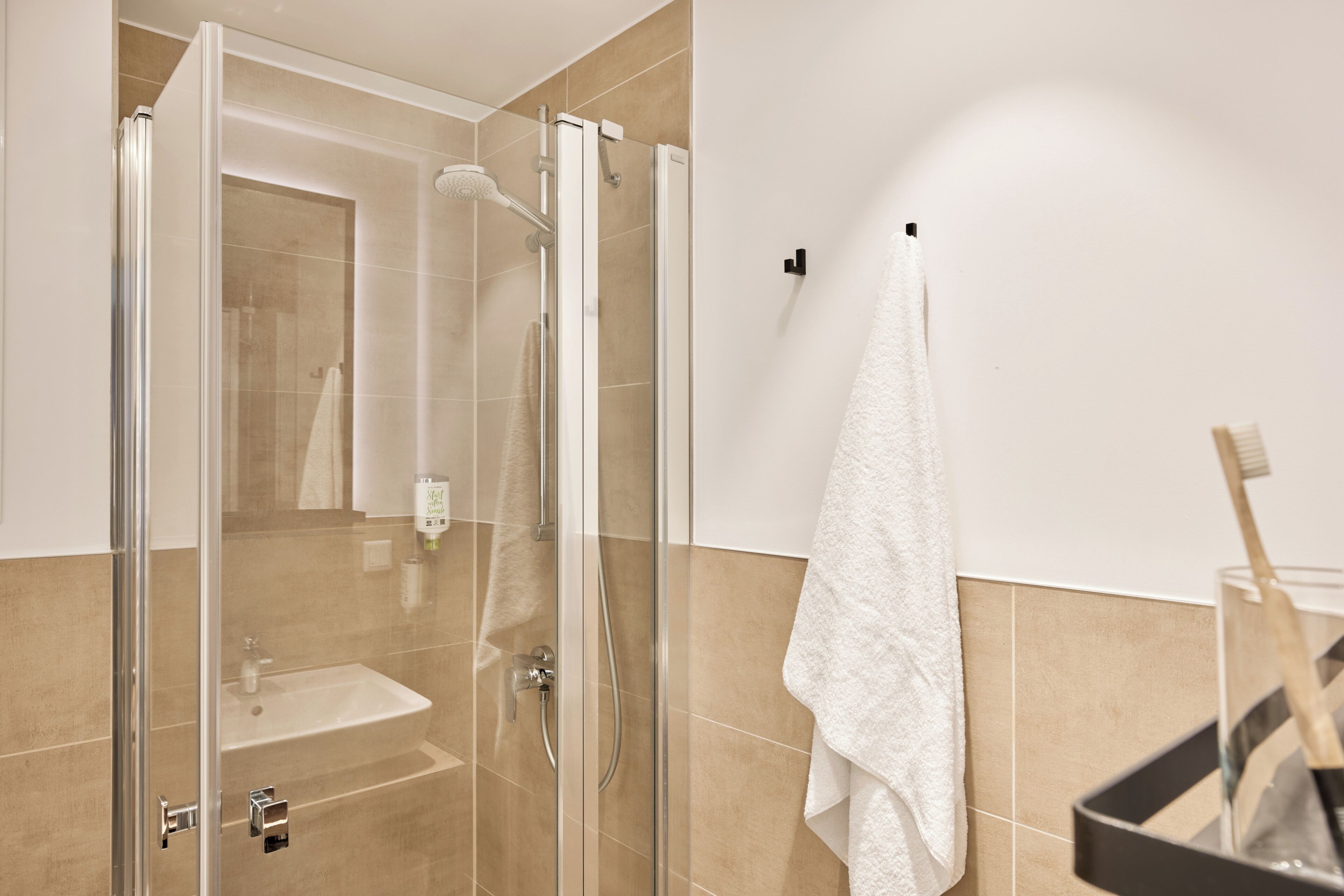 Un baño con ducha de mampara de vidrio, lavamanos y toalla colgada en un perchero.
