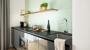 A modern kitchen with a built-in oven, a stainless steel sink, and a wooden shelf above the counter. - appartello - smarttime living Berlin (Berlin)