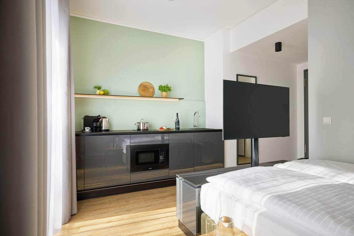 Quarto de hotel moderno com cozinha compacta, uma cama e televisão de tela plana.