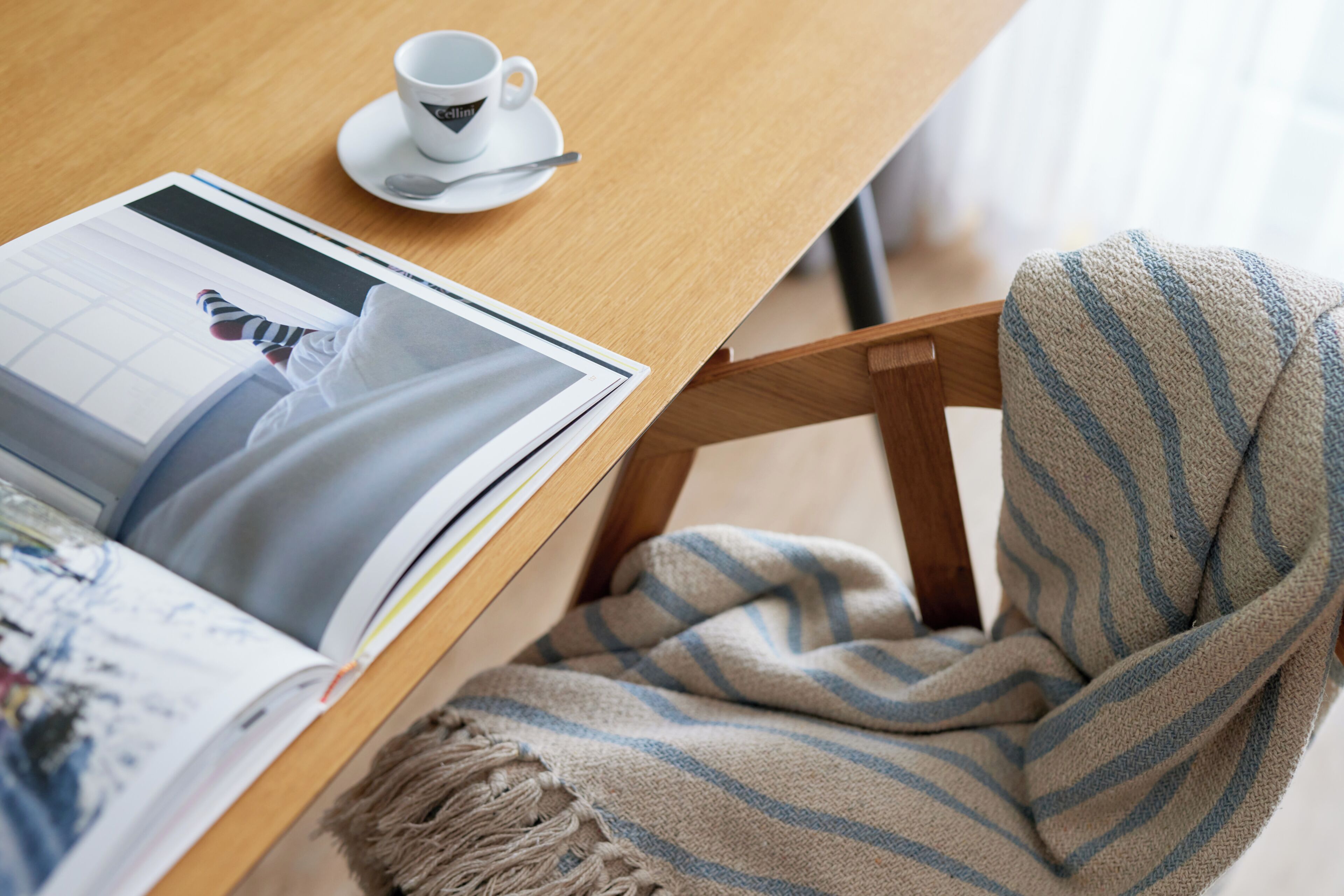 A wooden table with a magazine, a cup, and a striped chair.