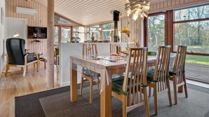 Een moderne eethoek met een houten tafel en stoelen, een televisie en een groot raam met uitzicht op de natuur.