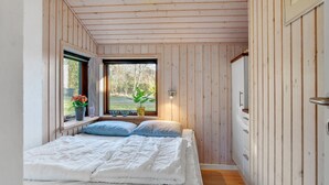 Een slaapkamer met een bed, een raam met uitzicht op groen, en een houten plafond.