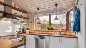 Een moderne keuken met houten balken, een groot raam met planten en een vaatwasser.