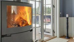 A modern room with a wood-burning stove, large glass doors leading to an outdoor deck, and a candle on a stand.