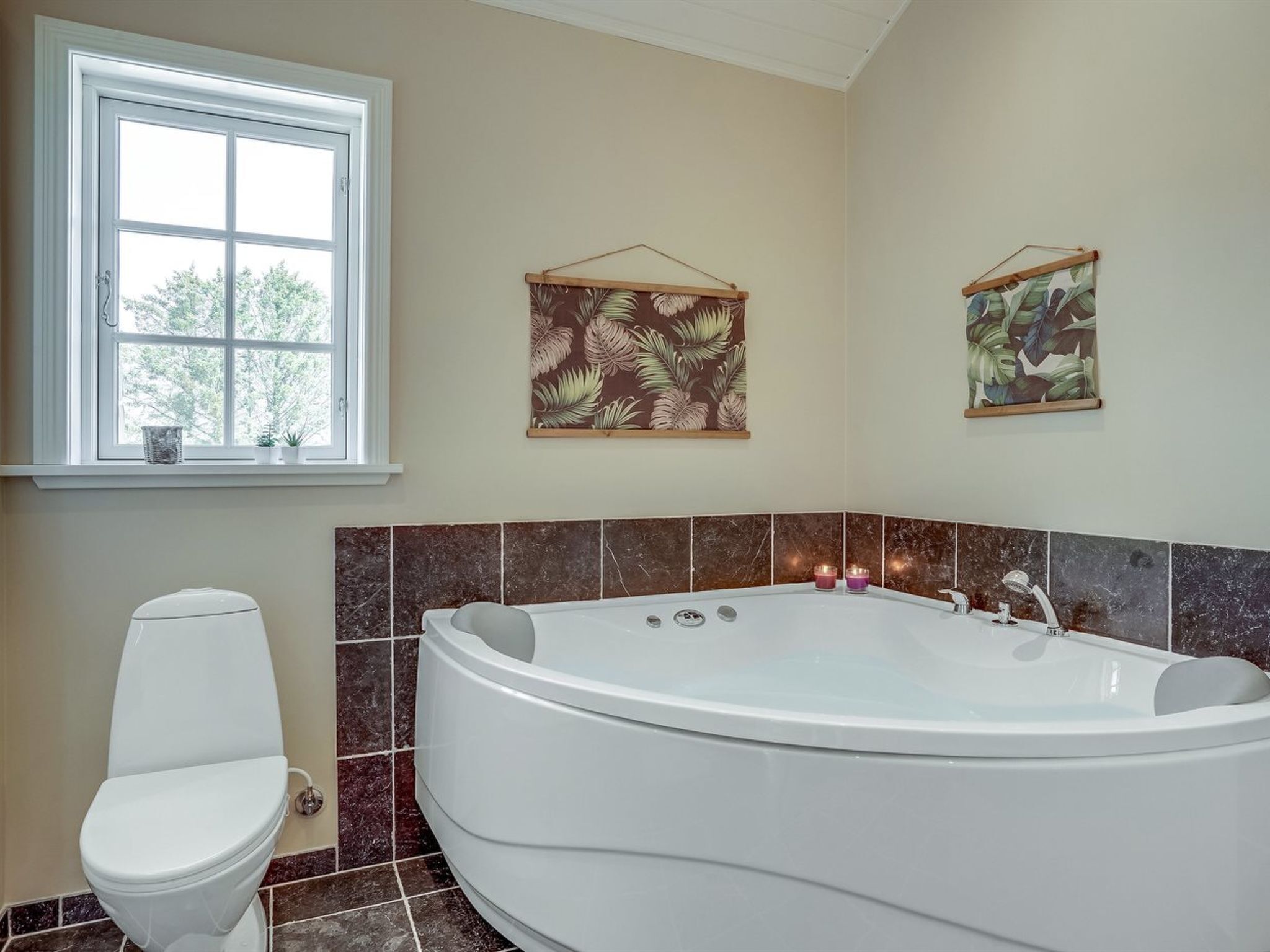 Ein Badezimmer mit einer freistehenden Badewanne, einer Toilette und zwei Wandregalen mit Kunstwerken im Blattmuster.