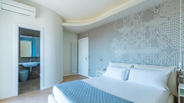 A modern bedroom with a large bed, a bathroom with a sink and mirror, and a decorative wall. - Casa di Cami by Wonderful Italy (Naples)