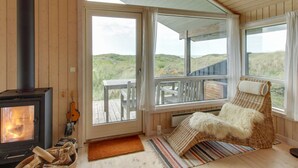Une pièce chaleureuse avec un poêle à bois, un fauteuil en osier et une vue sur l’extérieur.
