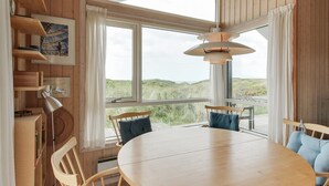 Un espace repas avec une table et des chaises en bois, de grandes fenêtres offrant une vue sur le paysage et un luminaire suspendu.