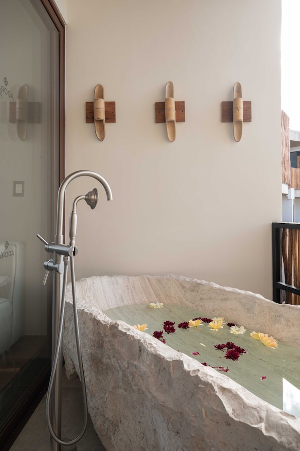 A bathroom with a stone bathtub, a shower, and wooden wall-mounted towel racks.