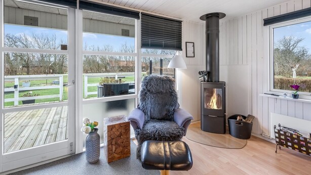 A cozy room with a fireplace, a plush chair, and large windows overlooking a deck. - "Fritzie" - 600m to the fjord by Interhome (Hemmet)
