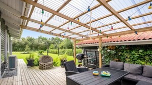 A covered patio area with a wooden deck, outdoor seating, and a grill. - "Fritzie" - 600m to the fjord by Interhome (Hemmet)
