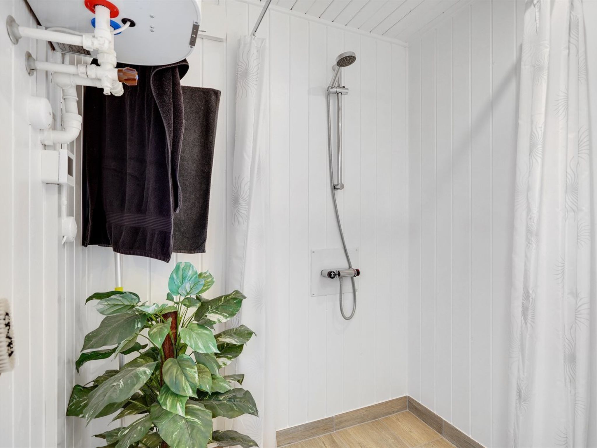 A bathroom with a shower, a towel rack, and a potted plant.